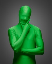 Thinking man with hand on chin wearing full green nylon bodysuit on a grey background