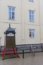 Old Swedish telephone box Rikstelefon in front of white wooden facade with mullioned windows in Vimmerby