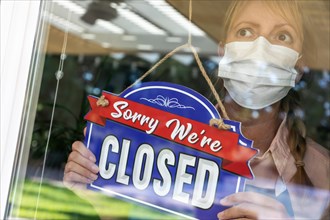 Female store owner wearing medical face mask turning sign to closed in window