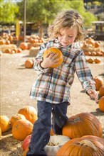 Adorable little boy sitting and holding his pumpkin in a rustic ranch setting at the pumpkin patch