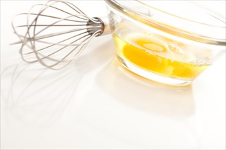 Hand mixer with eggs in a glass bowl on a reflective white background