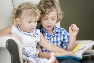 Cute young brother and sister reading a book together in a chair