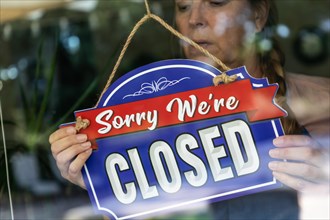 Sad female store owner turning sign to closed in window