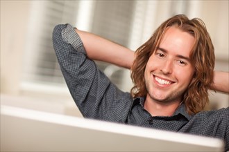Happy young man using A laptop computer with hands behind his head