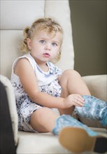 Adorable blonde haired blue eyed little girl putting on cowboy boots