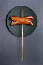 Fried sausage with wooden skewer on plate