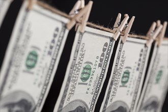 Hundred dollar bills hanging from a clothesline on a dark background
