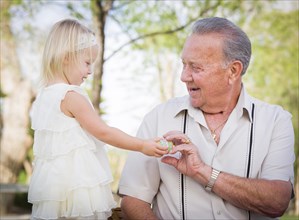 Cute baby girl handing easter egg to grandfather outside at the park