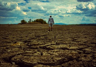 Man standing at cracked earth at the bottom dried up lake