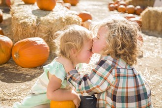 Sweet little boy kisses his baby sister in a rustic ranch setting at the pumpkin patch