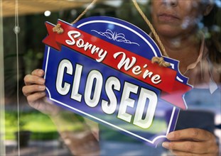 Sad female store owner turning sign to closed in window