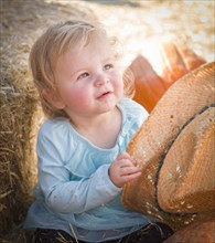 Adorable baby girl with cowboy hat in a country rustic setting at the pumpkin patch