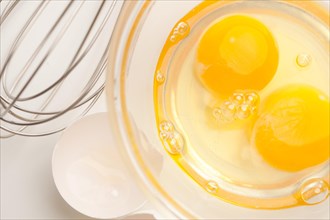 Hand mixer with eggs in a glass bowl on a reflective white background