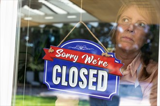 Sad female store owner turning sign to closed in window