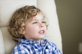 Cute young blonde boy daydreaming and sitting in chair