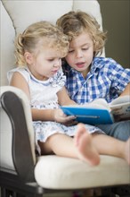 Cute young brother and sister reading a book together in a chair