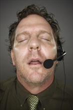 Businessman sleeps wearing a phone headset against a grey background