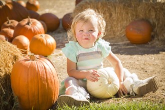 Adorable baby girl holding a pumpkin in a rustic ranch setting at the pumpkin patch