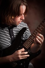 Young musician plays his electric guitar with dramatic lighting