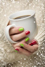 Woman in sweater with seasonal red and green nail polish holding a warm cup of coffee with snow flakes border