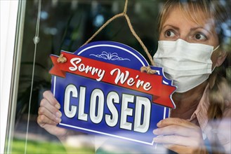 Female store owner wearing medical face mask turning sign to closed in window