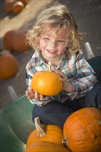 Adorable little boy sitting in wheelbarrow and holding his pumpkin in a rustic ranch setting at the pumpkin patch