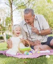 Loving grandfather and granddaughter coloring easter eggs together on picnic blanket at the park