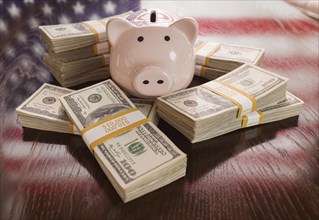 Thousands of dollars and piggy bank with reflection of american flag on table