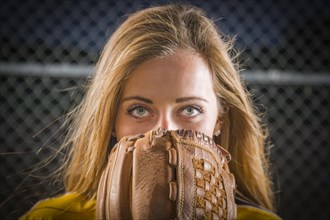 Dramatic young woman with softball glove covering her face outdoors