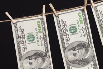 Hundred dollar bills hanging from a clothesline on a dark background