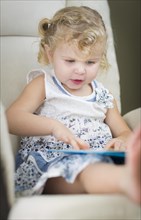 Adorable blonde haired blue eyed little girl reading her book in the chair
