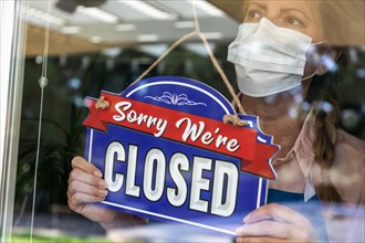 Female store owner wearing medical face mask turning sign to closed in window