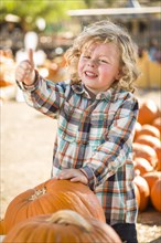 Adorable little boy leaning on pumpkin gives a thumbs up in a rustic ranch setting at the pumpkin patch