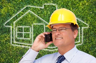 Contractor in hardhat on his cell phone over house icon and blurry grass