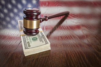 Wooden gavel resting on stack of money with american flag reflection on table