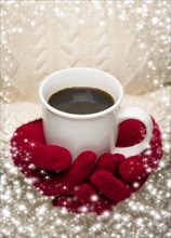 Woman in sweater with seasonal red mittens holding a warm cup of coffee with snow flakes border