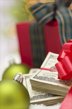Stack of one hundred dollar bills with red bow near green christmas ornaments and wrapped gift box on snow flakes