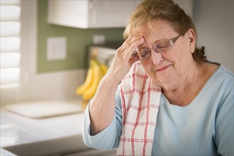 Sad crying senior adult woman at kitchen sink in home
