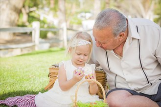 Loving grandfather and granddaughter enjoying easter eggs on a picnic blanket at park