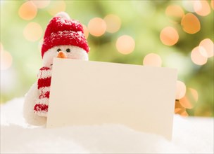 Cute snowman with scarf and hat next to blank white card over abstract background