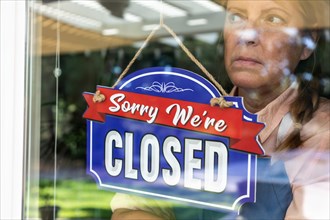 Sad female store owner turning sign to closed in window
