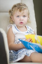 Adorable blonde haired blue eyed little girl reading her book in the chair