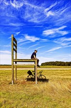 Cyclist sitting on oversized chair in a meadow