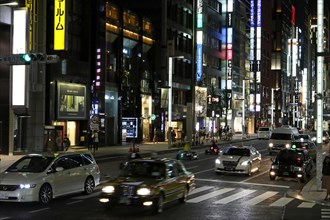 Illuminated street with neon lights and cars in traffic in Ginza district