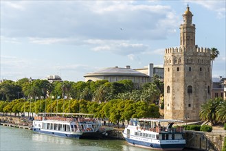View over the river Rio Guadalquivir on promenade with excursion boats and Torre del Oro