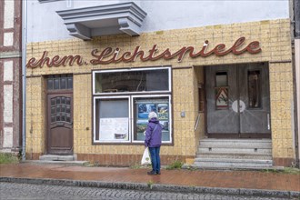 A woman stands in front of the shop window of the former cinema in Doemitz