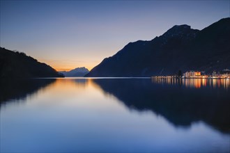 Illuminated lakeside promenade of Brunnen and view over Lake Lucerne at sunset with Mount Pilatus in the background