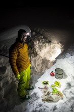 Man cooking with a camping stove in front of a snow cave