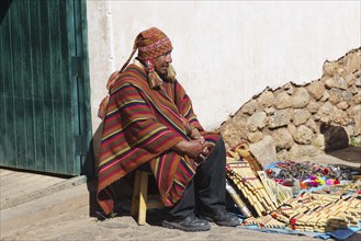 Indigenous man in colorful poncho with cap at his souvenir stand