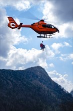 Two flight rescuers of the Bavarian Mountain Rescue Service hang on the wire rope of the rescue helicopter Christoph 14